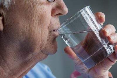 Persona mayor bebiendo agua de un vaso de cristal